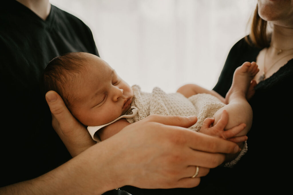 Detailaufnahme eines schlafenden Babys. Der kleine Junge liegt eingekuschelt in den Armen seiner Eltern.